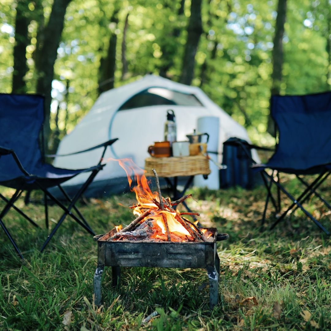 Camp fire in focus with chairs and a tent blurred in background